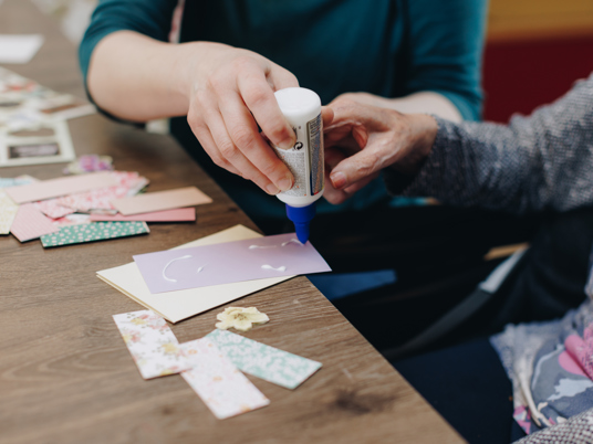 De Waterpoort Zorgpartners Bewoner Medewerker Welzijn Knutselen Papier Lijm Handen Close Up